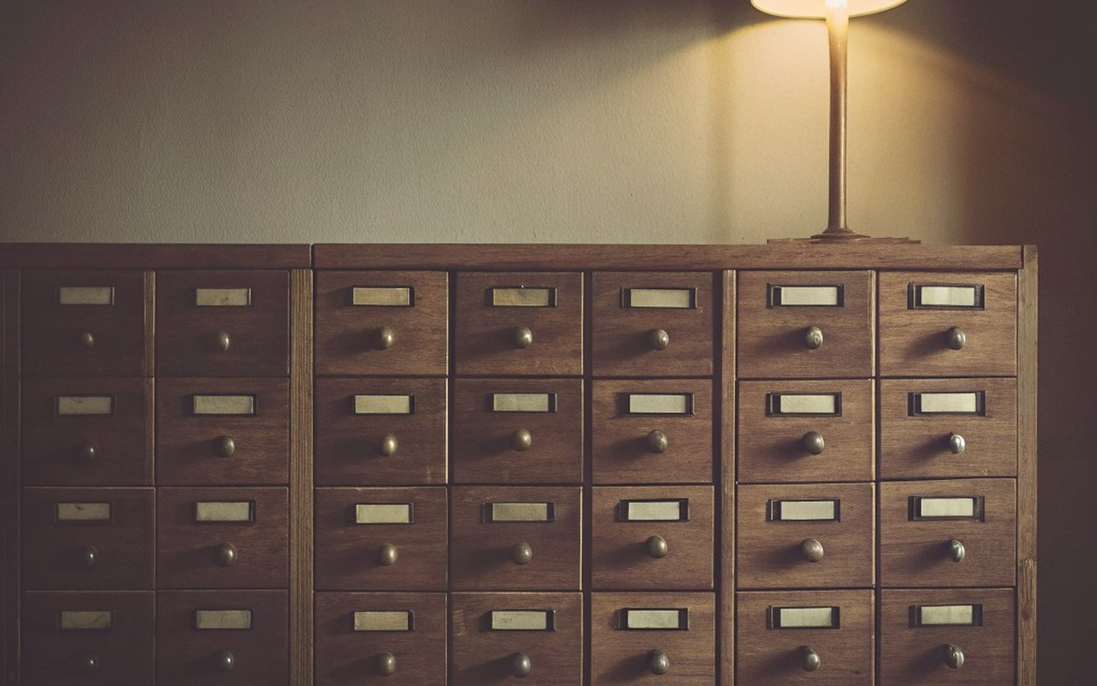A wooden card-catalogue cabinet under a desk lamp, every drawer labelled, a Quiet Build Field Notes image